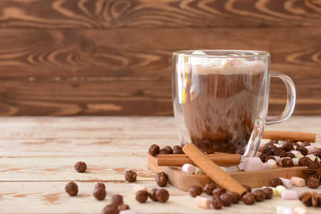 Tasty hot chocolate with cinnamon and marshmallows in cup on wooden background