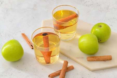 Tasty apple drink with cinnamon in glasses on light background