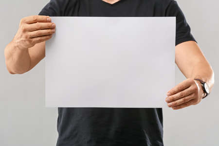 Man with blank paper sheet on gray background
