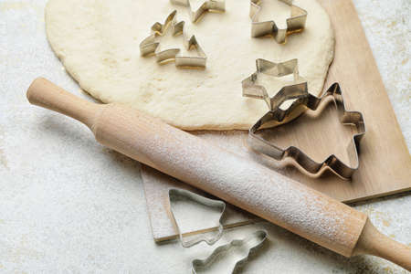 Cookie cutters, dough and rolling pin on light background