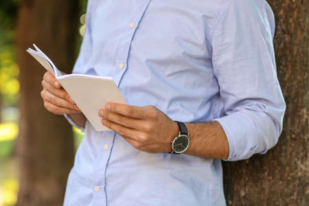 Young man reading magazine outdoors, closeup
