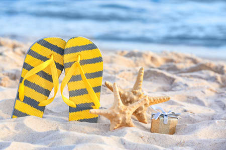 Flip-flops, starfish and gift on beach sand. Christmas vacation conceptの写真素材