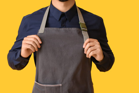 Young man wearing apron on color backgroundの写真素材