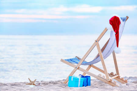 Beach chair, gifts and Santa hat on sea shore. Christmas vacation conceptの写真素材