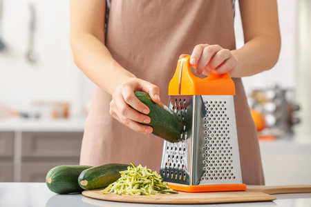 Woman grating zucchini in kitchenの写真素材