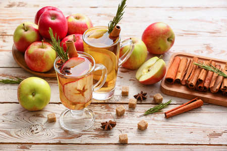 Tasty drink with spices and apple slices in cups on wooden backgroundの写真素材