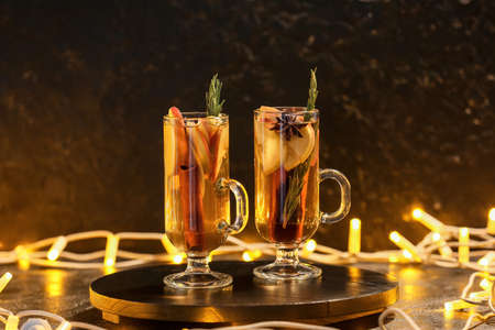 Tasty drink with spices and apple slices in cups on table at nightの写真素材