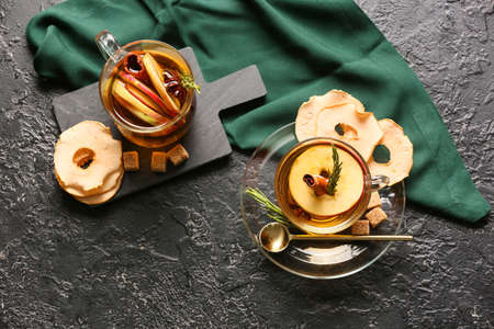 Tasty drink with spices and apple slices in cups on dark background