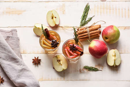 Tasty drink with spices and apple slices in glasses on light wooden backgroundの写真素材