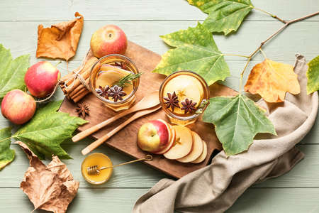 Tasty drink with spices and apple slices in glasses on color wooden background