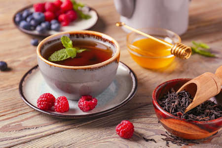 Cup of hot tea with mint and berries on wooden backgroundの写真素材