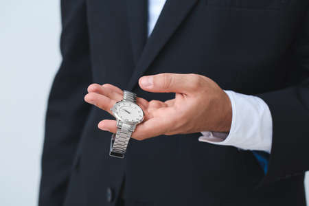 Young businessman holding stylish wristwatch on light backgroundの写真素材