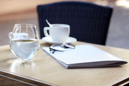 Blank magazine, glass of water and cup with coffee on table in cafe outdoorsの写真素材