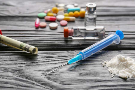 Syringe, drugs and money on wooden background