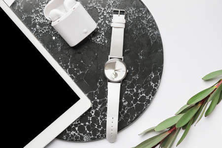 Stylish wristwatch, tablet computer and earphones on light background