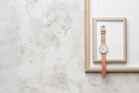 Stylish wristwatch and blank photo frames on light background