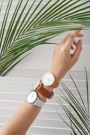 Female hand with stylish wristwatches and tropical leaf on light background