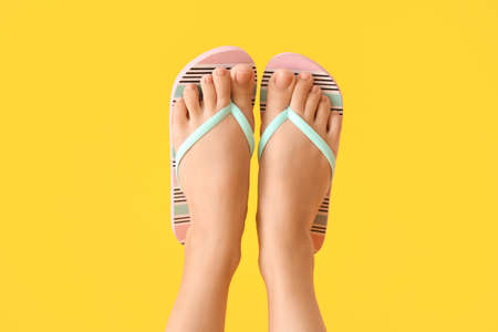 Legs of young woman in flip-flops on color background