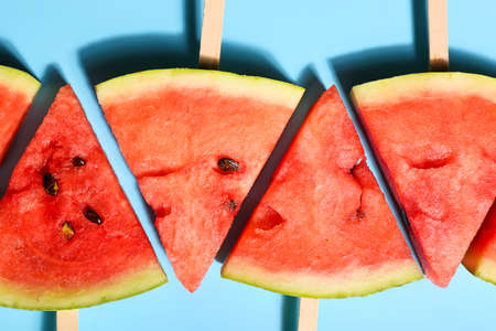 Slices of ripe watermelon with wooden sticks on color backgroundの写真素材