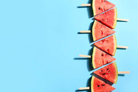 Slices of ripe watermelon with wooden sticks on color background