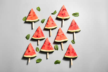 Slices of ripe watermelon with wooden sticks on gray background