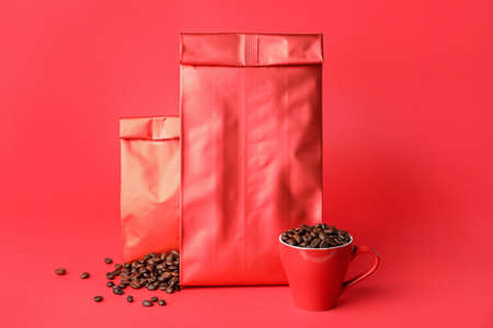 Bags and cup with coffee beans on color backgroundの写真素材