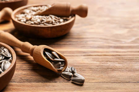 Bowls and scoops with sunflower seeds on wooden background