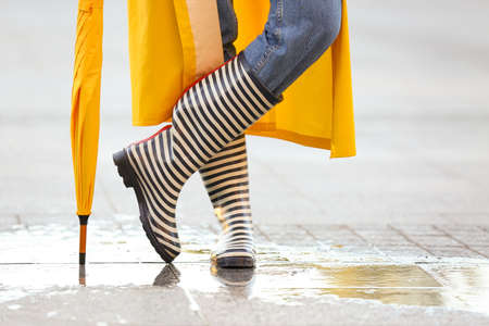 Beautiful young woman with umbrella wearing raincoat and gumboots outdoorsの写真素材