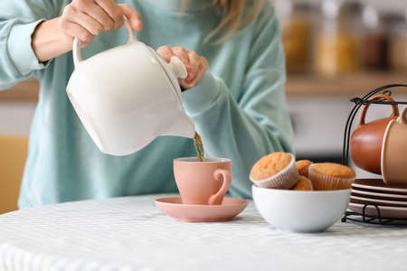 Woman pouring hot tea from teapot into cup at tableの写真素材