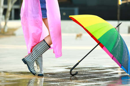 Beautiful young woman with umbrella wearing raincoat and gumboots outdoorsの写真素材