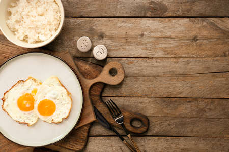 Plate with tasty eggs and rice in bowl on wooden backgroundの写真素材