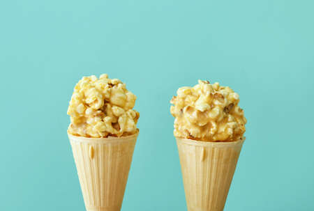 Waffle cones with popcorn balls on color background