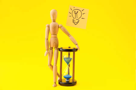 Wooden mannequin, hourglass and drawn light bulb on color background