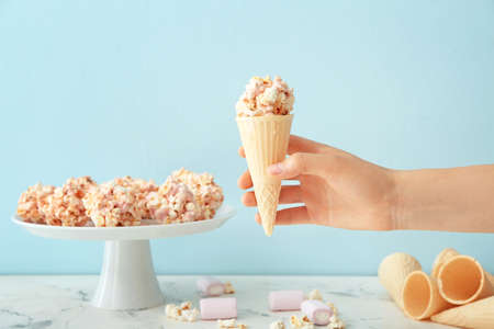 Woman holding waffle cone with popcorn ball on color background