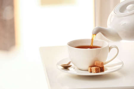 Pouring tea from teapot into cup on light table