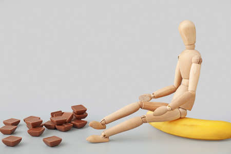 Wooden mannequin and banana and chocolate on light background