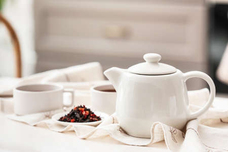 Teapot and dry tea leaves on light table in room