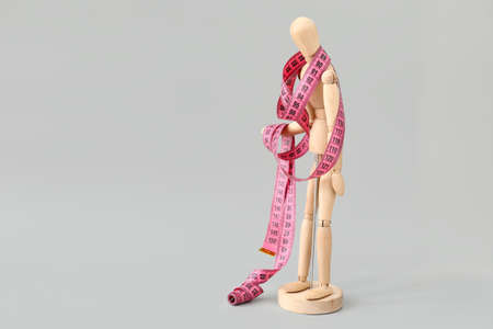 Wooden mannequin with measuring tape on light background