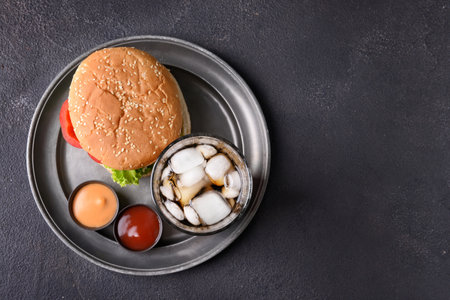 Tray with tasty burger, sauces and cola drink on dark backgroundの写真素材