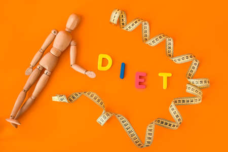 Wooden mannequin with measuring tape and word DIET on color backgroundの写真素材