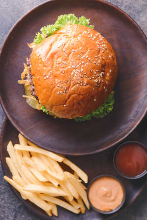 Plates with tasty burger, sauces and french fries on table, closeup
