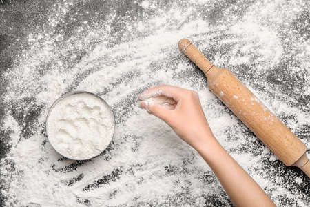 Female hand with flour and rolling pin on dark backgroundの写真素材