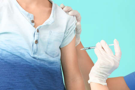 Doctor giving diabetic boy insulin injection on color background
