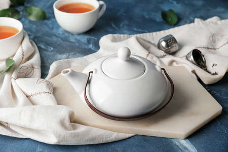 Teapot and cups of tea on color background