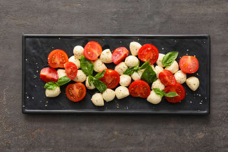 Plate with mozzarella cheese, tomatoes and basil on dark backgroundの写真素材