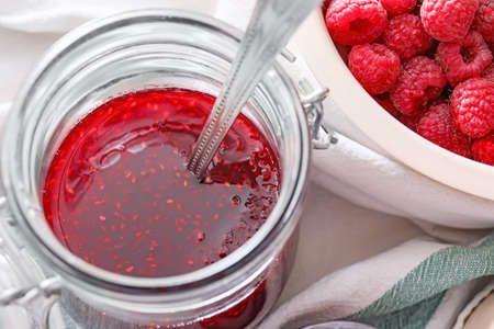 Glass jar with sweet raspberry jam on table