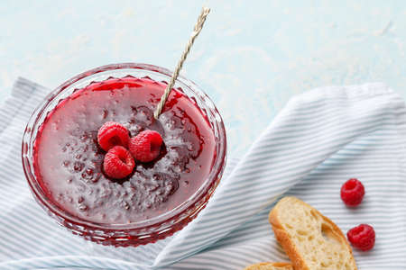 Bowl with sweet raspberry jam on light background