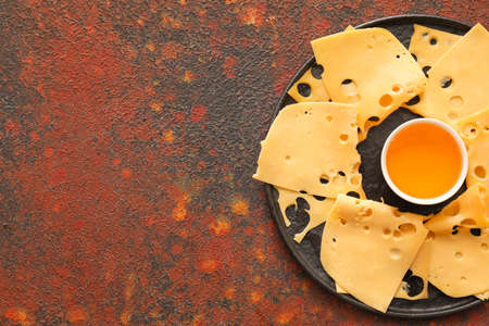 Plate with slices of tasty cheese and honey on grunge backgroundの写真素材