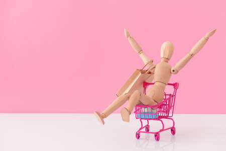 Wooden mannequin with shopping cart on color background