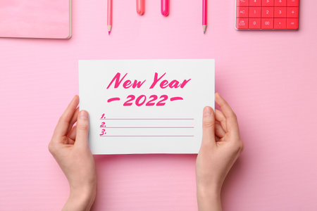 Young woman making to do list for 2022 against color background